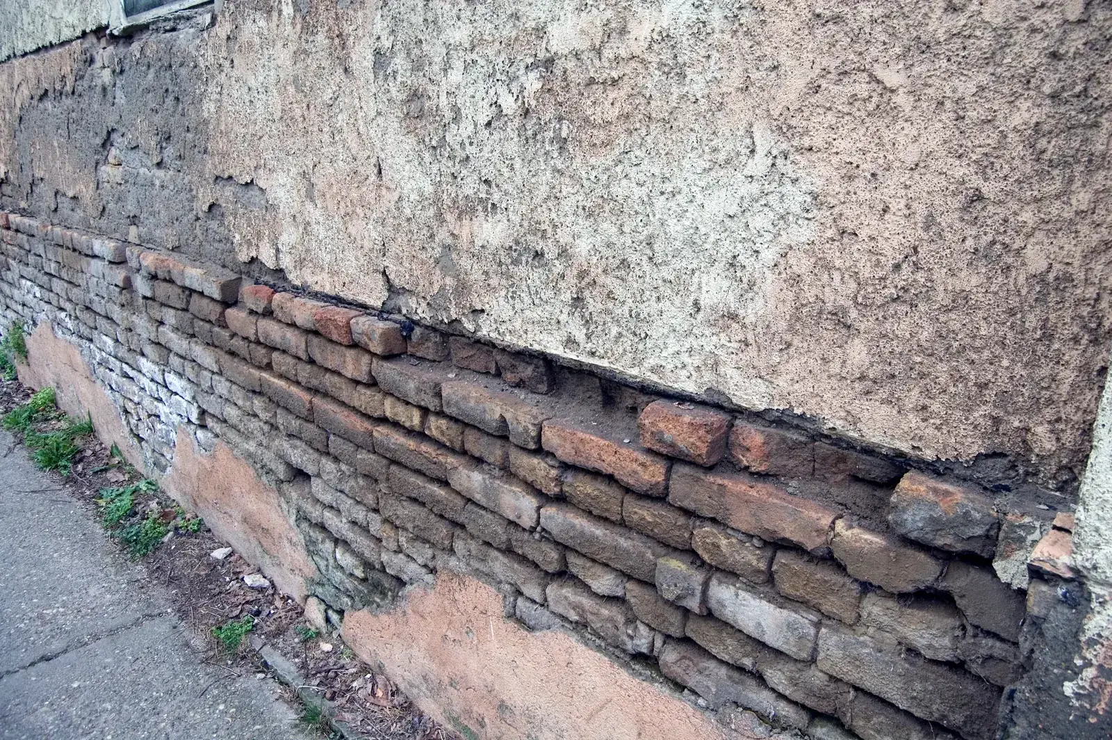 Cracked and crumbling render exposing the brick base of an older home