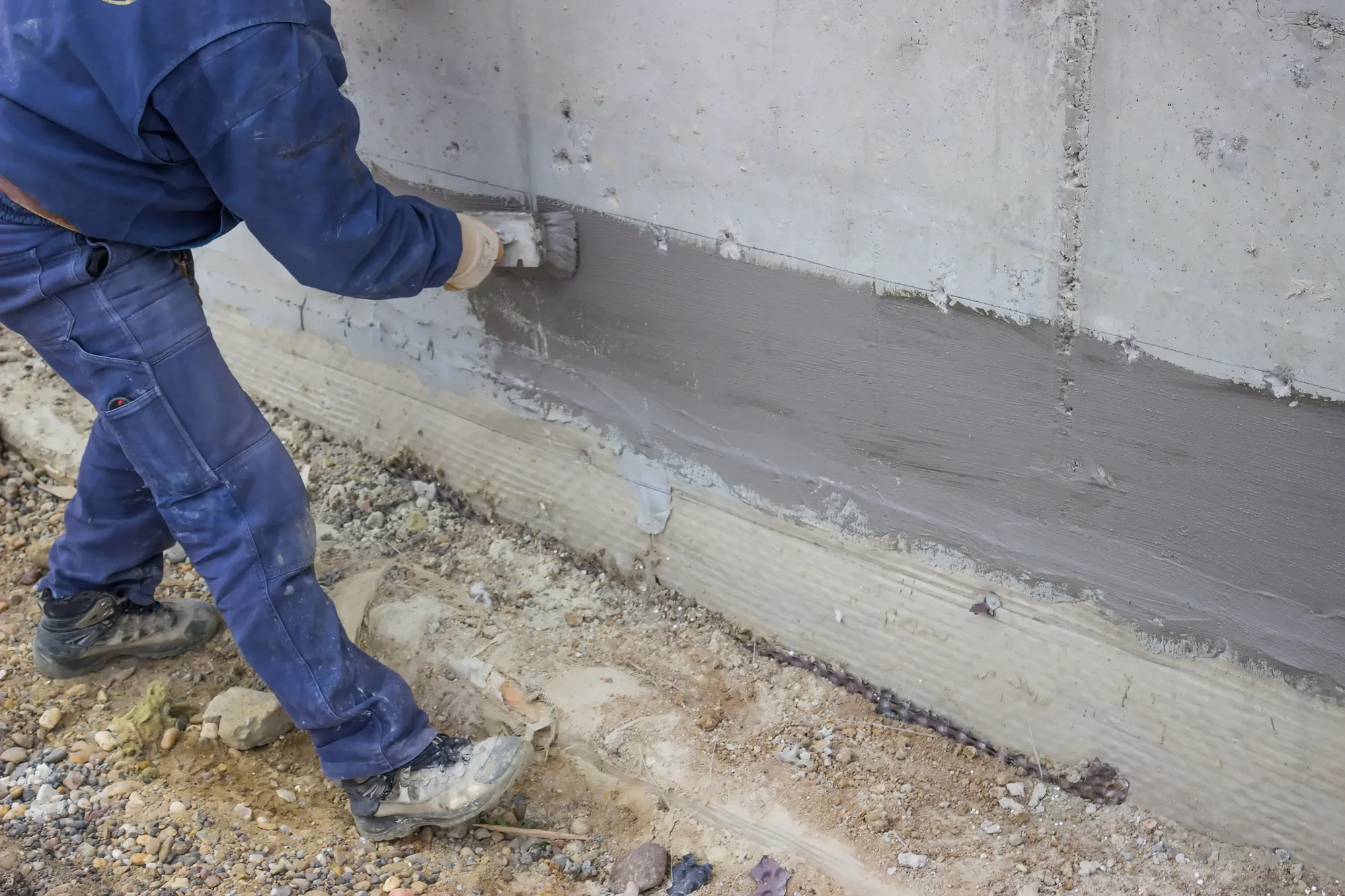 Worker applying a cement-based coating to a concrete foundation wall