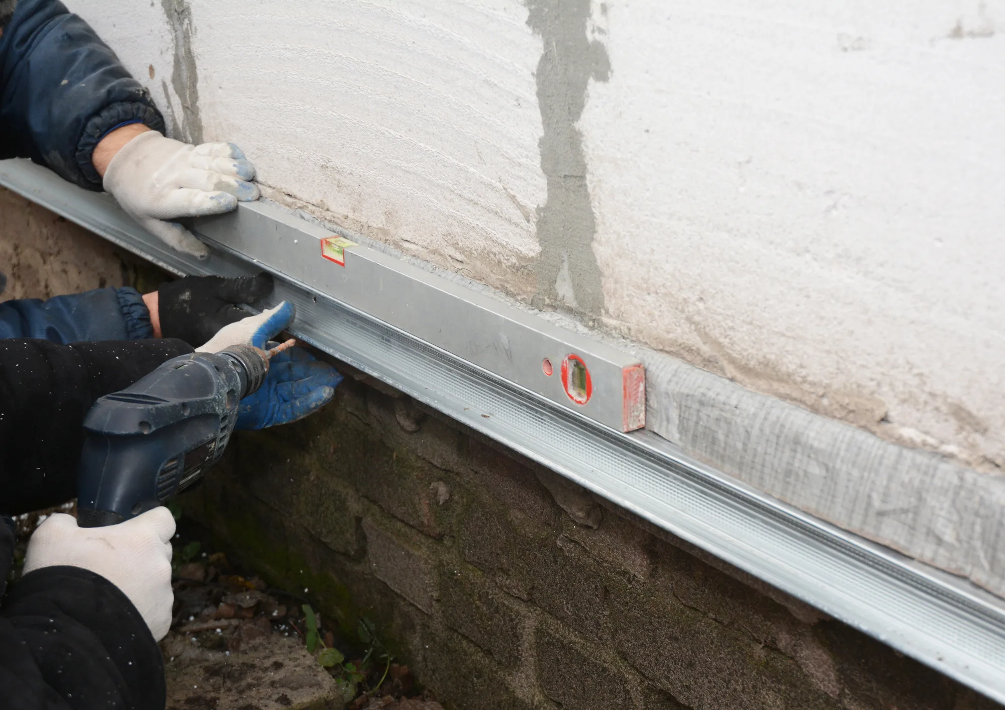 Tradesmen fixing a steel reinforcement angle along a foundation wall with a spirit level