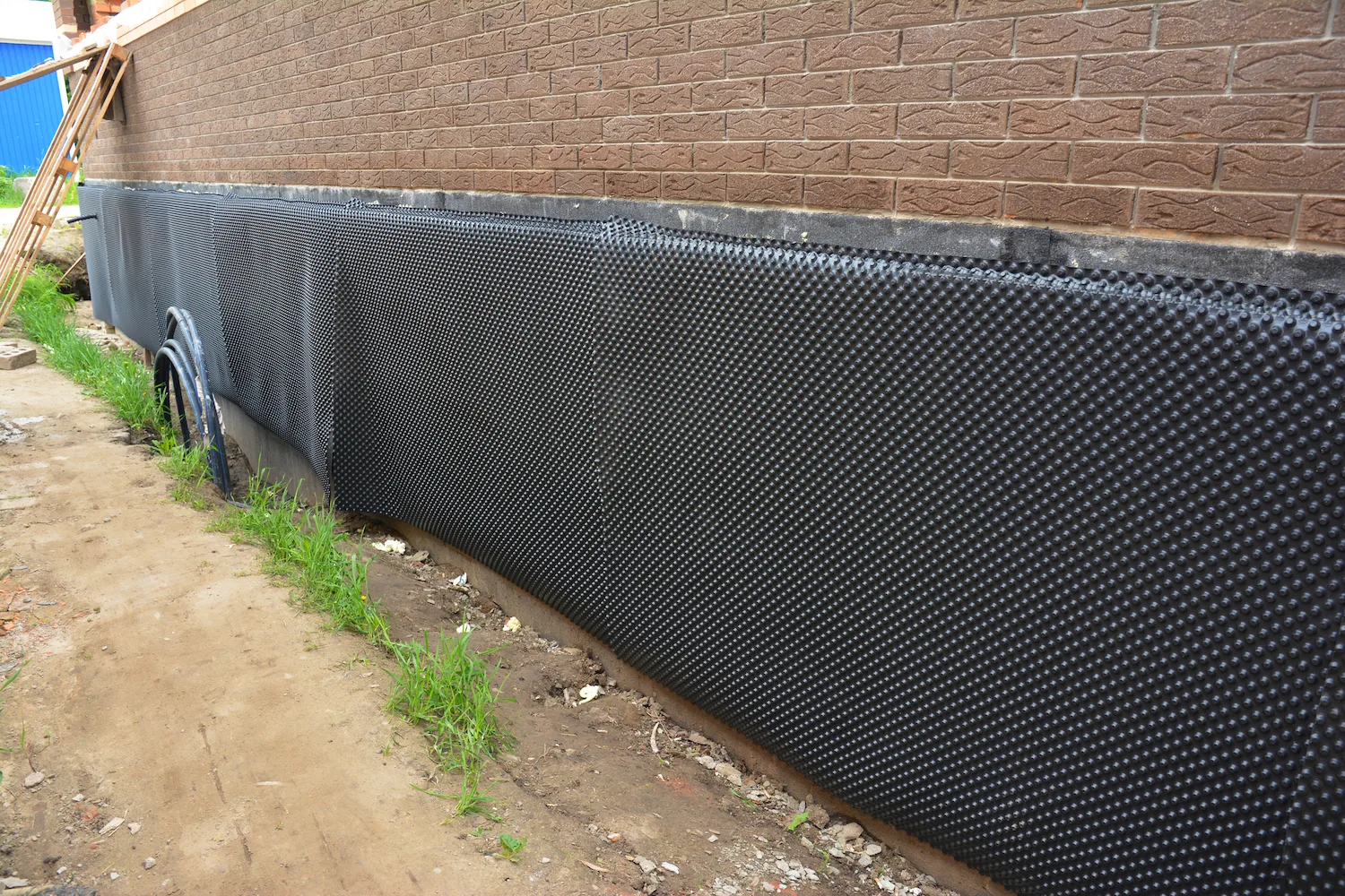 Dimpled waterproofing membrane fitted along the base of a brick wall